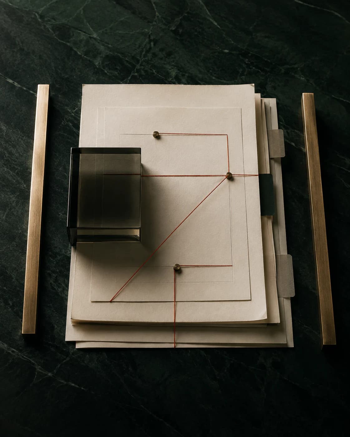 Agreement papers, smoked glass and a precise coral thread arranged on deep-green stone